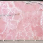 Large polished pink onyx slab with natural white veining and translucent rose pink patterns displayed in a stone warehouse
